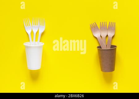 Plastic and eco-friendly disposable utensils made of bamboo wood and paper on yellow background. Forks and cups. Ecology problem, zero waste concept. Stock Photo