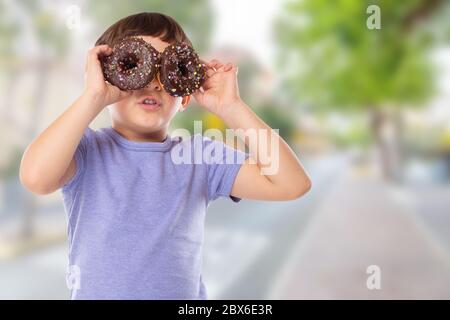 Little boy child with donuts donut having fun happy happiness town unhealthy eating outdoors Stock Photo