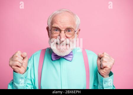 Closeup photo of crazy grandpa negative facial expression grimace outraged raise fists grinning wear specs mint shirt suspenders violet bow tie Stock Photo