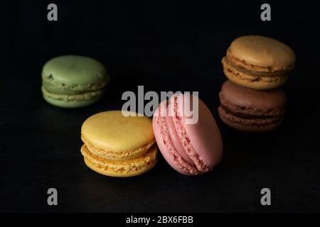 Five colored macarons on a black background, with low key lighting. closeup two in balance with strawberry and vanilla flavor Stock Photo