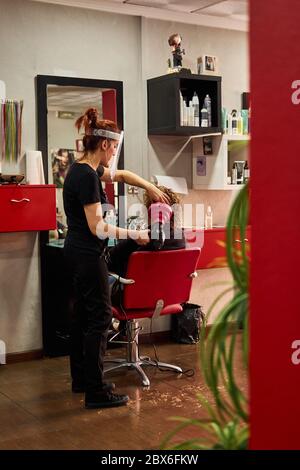 Hairdresser with a face shield dries her client's hair in her salon Stock Photo