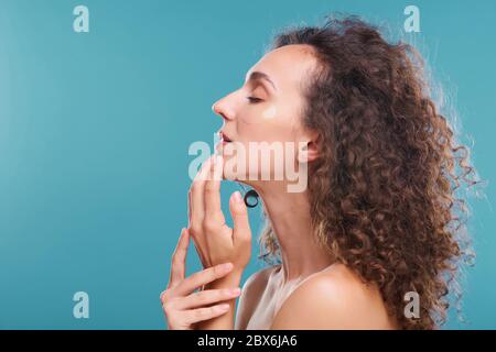 Profile of young beautiful female with long dark wavy hair enjoying feeling of freshness on her face during undereye skincare procedure Stock Photo