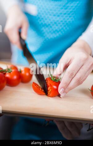Housewife cutting cherry tomato slices on kitchen table. Vegetarian food meal preparing. Stock Photo