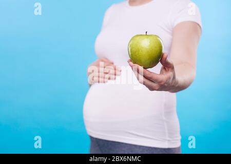 Hand of young healthy pregnant woman giving or showing you fresh granny smith apple while standing in front of camera Stock Photo
