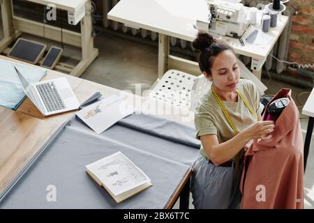 Young modern worker of fashion design studio sewing clothing item on dummy while working over new seasonal collection in workshop Stock Photo