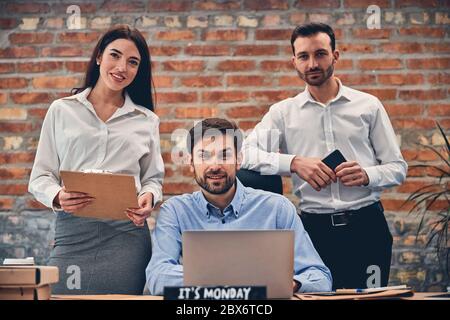 Teammates working at laptop in modern office against brick wall Stock Photo