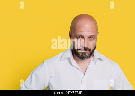 Serious middle-aged man with folded arms and a deadpan expression posing in front of a yellow background Stock Photo