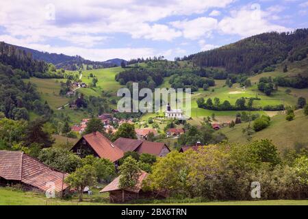 Beautiful view on green hills. Idyllic rural scene. Blue sky, mountains  view with forest, green meadows and small town in the valley. Houses with the Stock Photo