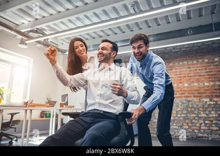 Happy co-workers racing on chairs in modern office Stock Photo