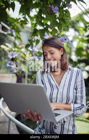 young caucasin female watching her laptop, smiling, at botanical garden Stock Photo