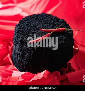 Creative Black Cake Decorated With Red Cayenne Pepper on Red Bright Background. Cake And Bake With Passion. Stock Photo