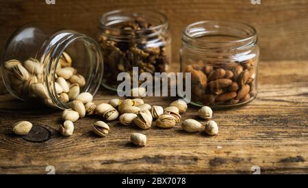 Pistachios scattered on the vintage table from a jar and with other nuts on background. Pistachio is a healthy vegetarian protein nutritious food Stock Photo
