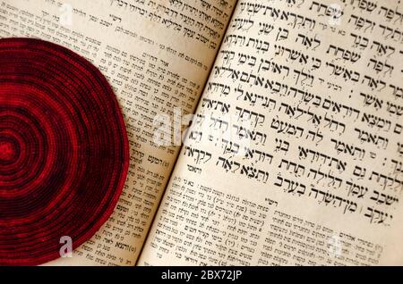 An opened old Jewish Bible and red knitted jewish bale. Selective focus. Closeup of hebrew text Stock Photo