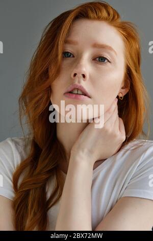 Portrait of a beautiful redhead girl with clean skin, blue eyes and freckles in a white T-shirt looking into the frame.  Stock Photo