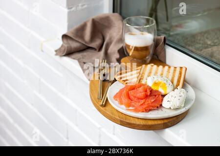 Poached egg with smoked salmon, toasted bread and coffee on white windowsill outside the building. Stock Photo