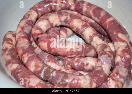 Making homemade sausage at home. Stuffing pork intestine with meat and fat. The photo shows the stage when the already stuffed raw sausage is rolled i Stock Photo