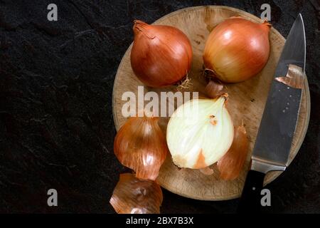 Cutting onions on round wooden vintage board.  Top view, on slate. Stock Photo