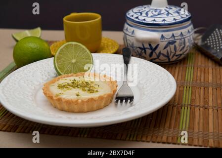 Side view of lemon tart on dish plate with lemon slices on table. Lemon tartlet with zest on top. Strawberry Pastry. Sweet with citrus fruit. Selectiv Stock Photo