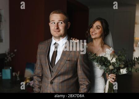 Smiling bride with wedding bouquet stroking the astonished groom on the shoulder. Bride and groom portrait Stock Photo
