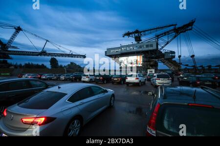 05 June 2020, Saxony-Anhalt, Gräfenhainichen: Visitors stand with their cars in a drive-in cinema between former large-scale equipment from the open-cast lignite mine in Ferropolis. From now on, films for children and adults will be shown regularly on the 90 square meter LED wall. There will also be concerts. The film 'Gundermann' will be shown at the beginning. The story of the singing excavator driver was partly shot in Ferropolis. Photo: Jan Woitas/dpa-Zentralbild/dpa - ATTENTION: Only for editorial use in connection with current reporting and only with unchanged image detail Stock Photo