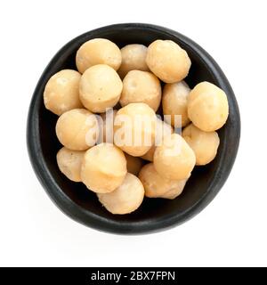Macadamia nuts in rustic black bowl.  Top view, isolated on white. Stock Photo