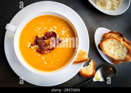 Pumpkin soup with bacon, parmesan and garlic bread.  Top view, over dark slate. Stock Photo