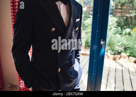 Closeup shot of elegant man in business suit. Dark blue jacket with anchor decorated buttons. Gentleman standing at glass doors. Stock Photo