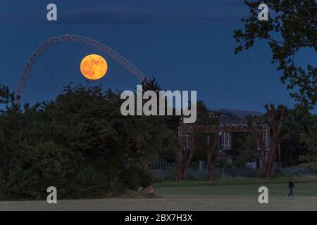 Wembley, UK.  5 June 2020. UK Weather - A person walks by in a field as June's full moon, known as a Strawberry Moon, rises behind Wembley Stadium in north west London.  June's full moon, according to The Old Farmer's Almanac, was the signal for Native American Algonquin tribes to harvest wild strawberries.  This month's full moon also coincides with a subtle penumbral eclipse, which occurs when the Earth casts a slight shadow over the Moon.    Credit: Stephen Chung / Alamy Live News Stock Photo