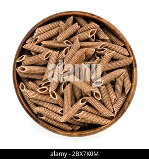 Wholemeal penne pasta in wooden bowl.  Top view, isolated on white. Stock Photo