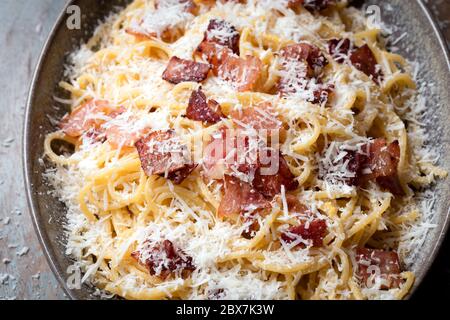 Spaghetti carbonara, top view, in oval dish on rustic timber table. Stock Photo