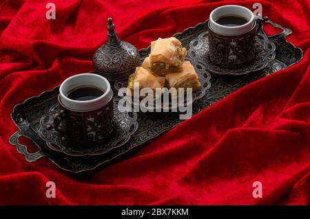 Ramadan treat and arabian hospitality concept with turkish baklava and mini coffee cups on authentic mediterranean metal tray isolated on red velvet f Stock Photo