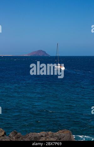 A pleasure boat with sails lowered in a calm sea near the coast of some islands Stock Photo