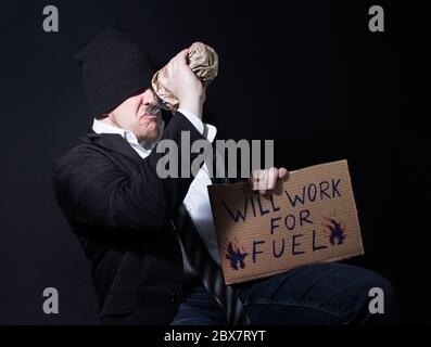 hoto of a alchoholic homeless business man drinking from a bootle and sitting with cardboard sing. Stock Photo