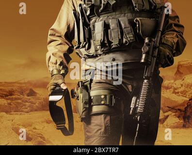 Photo of a soldier in military outfit standing on orange desert background. Stock Photo