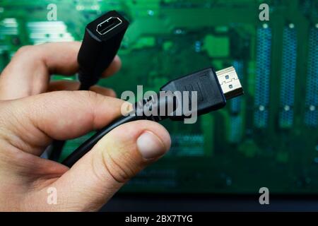 First person view hand holding HDMI cable on computer circuit board. Stock Photo