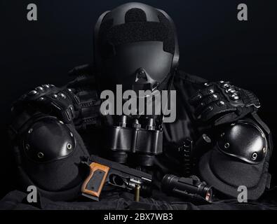 Black military tactical gun, helmet, glowes, cartridge belt, bandolier, gun shell, knife, binocular and knee protection laying on a black table. Stock Photo