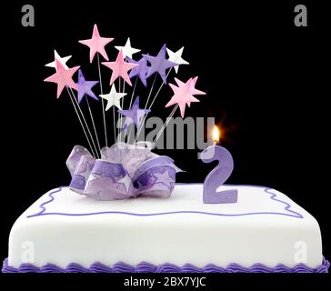 Fancy cake with number 2 candle.  Decorated with ribbons and star-shapes, in pastel tones on black background. Stock Photo