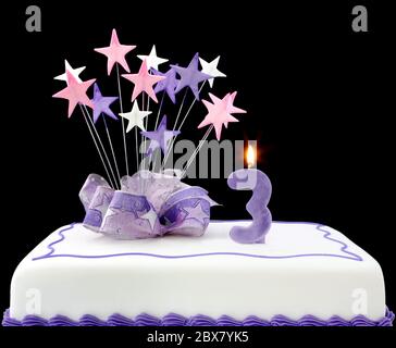 Fancy cake with number 3 candles.  Decorated with ribbons and star-shapes, in pastel tones over black background. Stock Photo