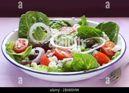 Greek salad in old enamel bowl.  Delicious romaine lettuce, cherry tomatoes, crumbled feta cheese, cucumber and black kalamata olives. Stock Photo