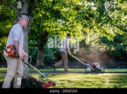 two men weed eating and mowing yard for landscaping job in Kentucky Stock Photo