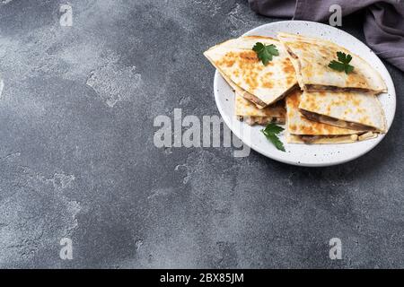 Pieces of quesadilla with mushrooms sour cream and cheese on a plate with parsley leaves. Concrete background copy space Stock Photo