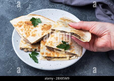 Pieces of quesadilla with mushrooms sour cream and cheese on a plate with parsley leaves. Concrete background close up Stock Photo