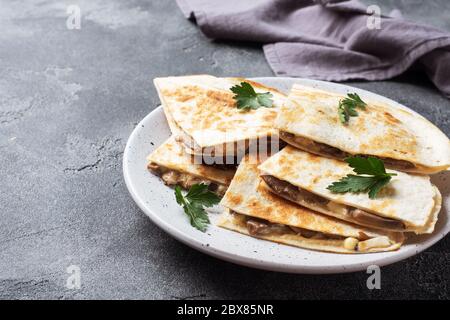Pieces of quesadilla with mushrooms sour cream and cheese on a plate with parsley leaves. Concrete background copy space Stock Photo