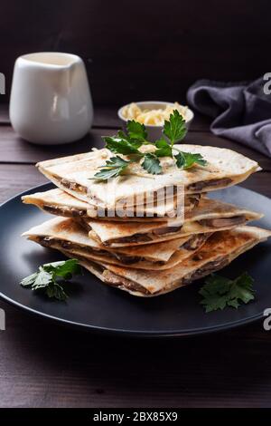 Pieces of quesadilla with mushrooms sour cream and cheese on a plate with parsley leaves. Wooden background close up Stock Photo