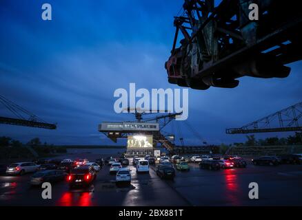 05 June 2020, Saxony-Anhalt, Gräfenhainichen: Visitors stand with their cars in a drive-in cinema between former large-scale equipment from the open-cast lignite mine in Ferropolis. From now on, films for children and adults will be shown regularly on the 90 square meter LED wall. There will also be concerts. The film 'Gundermann' will be shown at the beginning. The story of the singing excavator driver was partly shot in Ferropolis. Photo: Jan Woitas/dpa-Zentralbild/dpa - ATTENTION: Only for editorial use in connection with current reporting and only with unchanged image detail Stock Photo