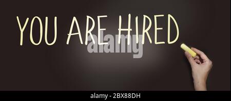 You are hired words written on blackboard and hand with pale yellow chalk. Career development business management crisis unemployement freelance job Stock Photo