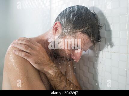 home bathroom dramatic portrait of young attractive sad and depressed man in the shower leaning against the wall thoughtful feeling overwhelmed by lif Stock Photo