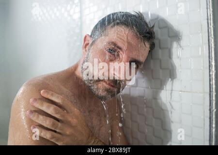 home bathroom dramatic portrait of young attractive sad and depressed man in the shower leaning against the wall thoughtful feeling overwhelmed by lif Stock Photo