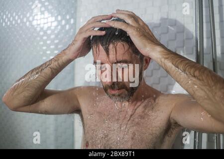 home bathroom dramatic portrait of young attractive sad and depressed man in the shower suffering depression crisisl feeling overwhelmed by life probl Stock Photo