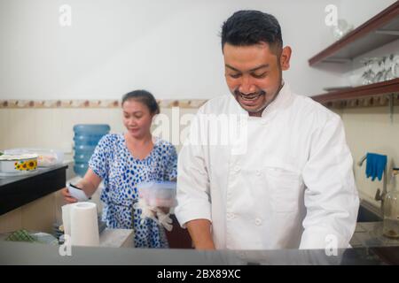 happy Asian couple cooking together -  home kitchen lifestyle portrait of Chinese cheerful and sweet husband and wife making delicious traditional Jap Stock Photo